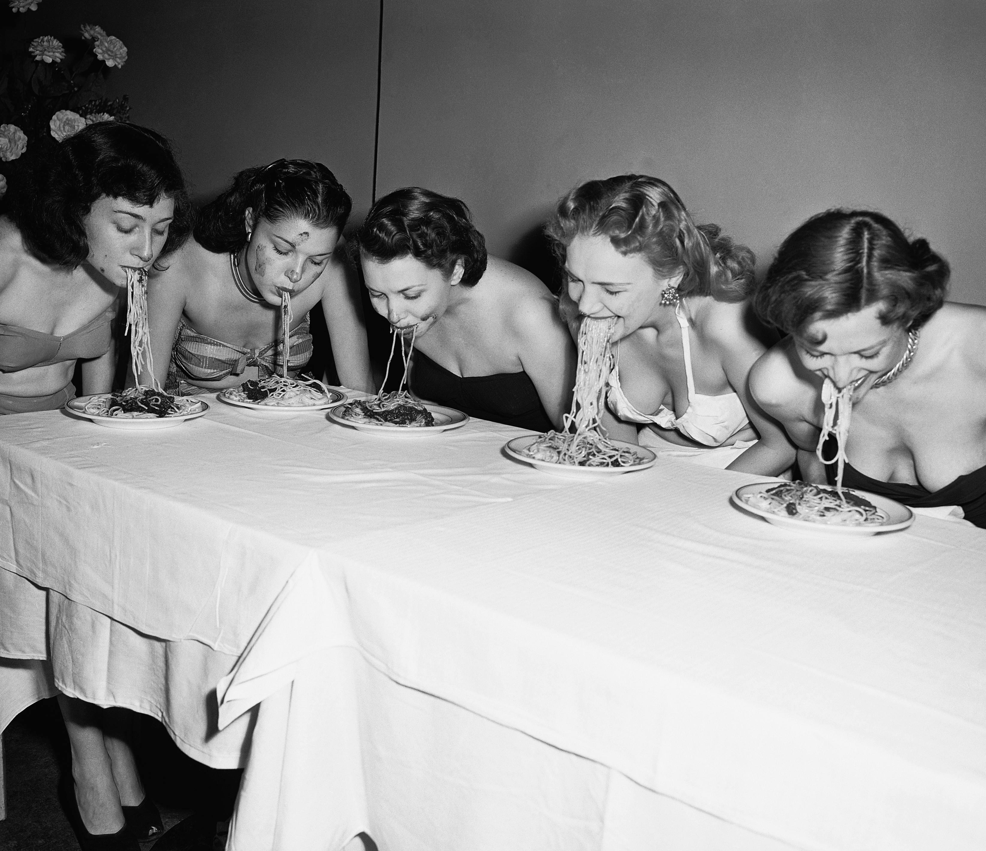 eating fun rivalry women head and shoulders portrait caucasian ethnicity dinner plate competitor flower arrangement spaghetti tablecloth american eating contest swimwear five people new york city table human person